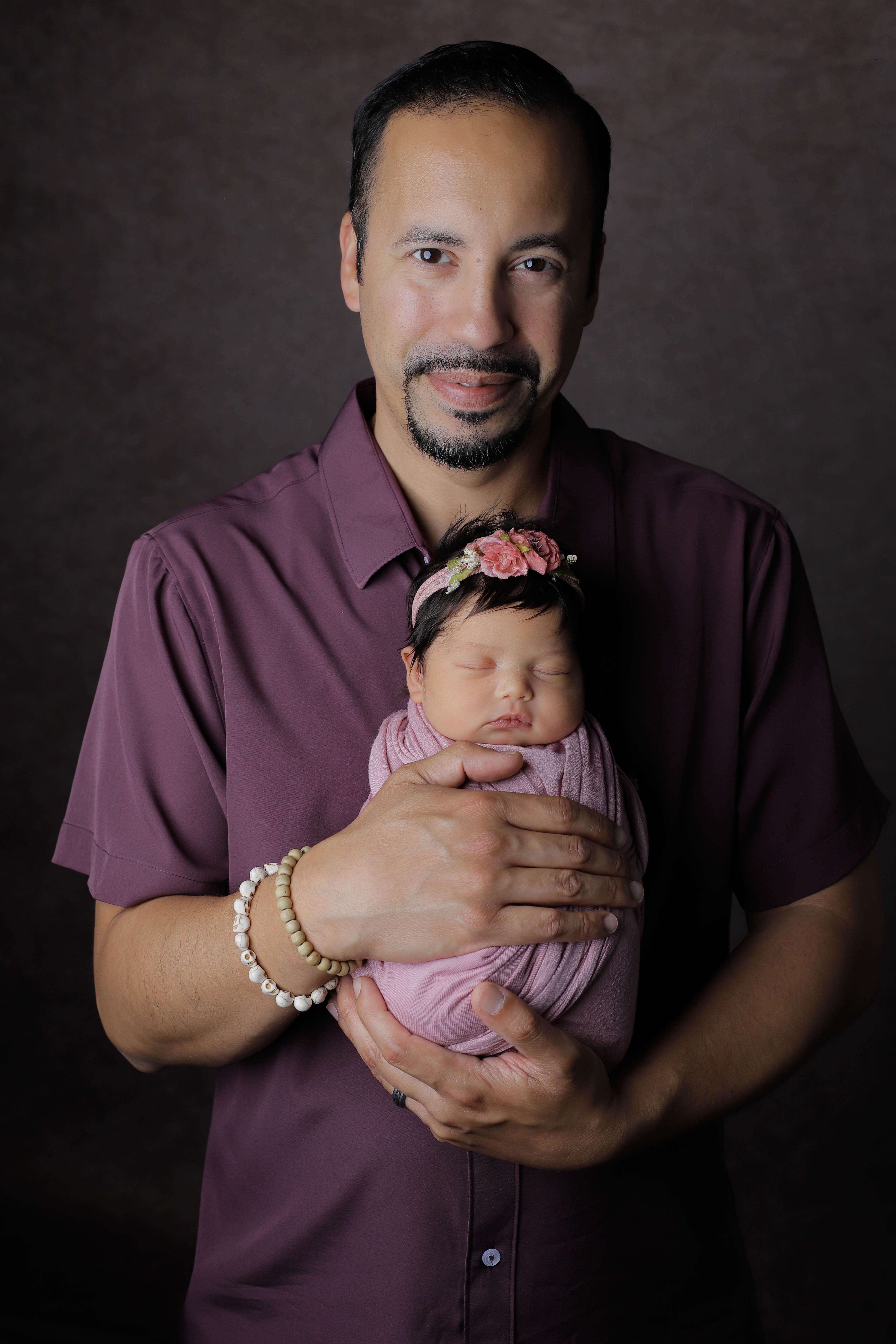 A newborn baby wrapped in soft pink, eyes gently closed, posed peacefully on a creamy textured blanket.